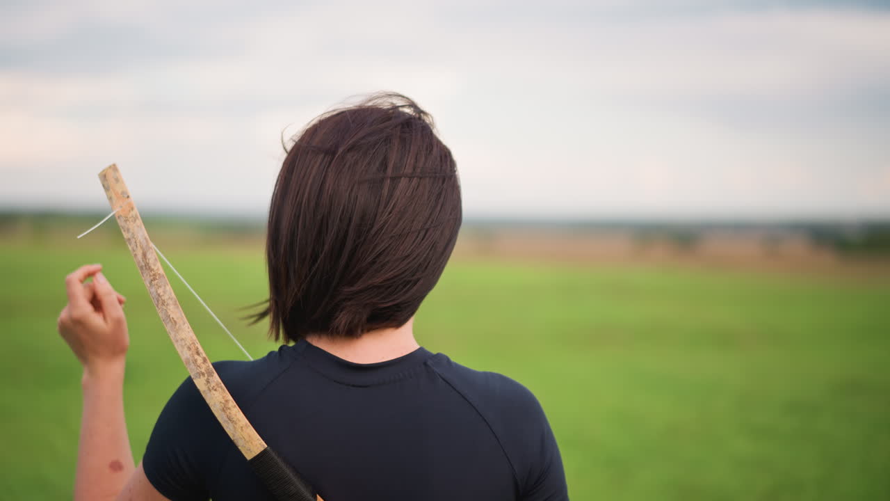 solo figure with wooden staff meadow. contemplative warrior stance back to camera, leather jacket hint, overcast sky and distant horizon, wind stirring hair, slow training motion, rustic cinematic