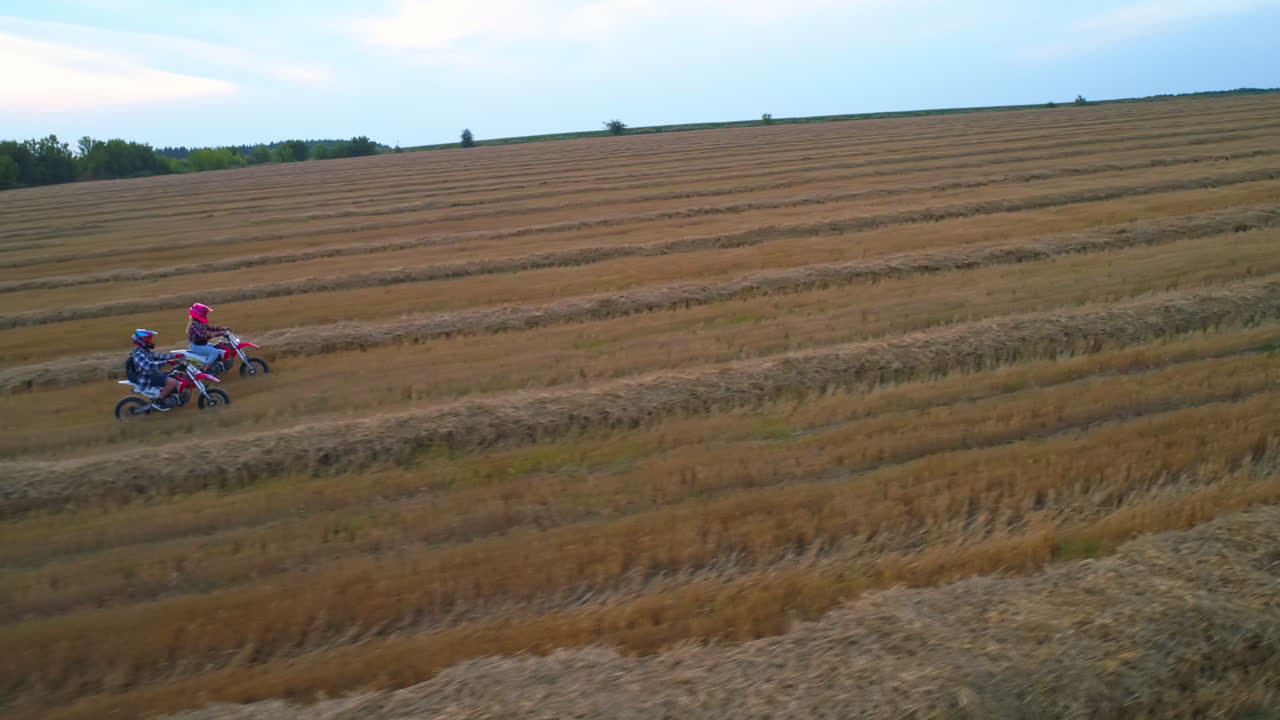 Happy young couple having fun riding motorbikes outside the city. Pair go by motorcycles wearing helmets. Mowed wheat field at backdrop.