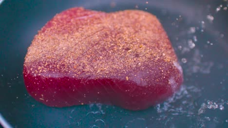 un pedazo de filete de atún rojo con condimentos que se arroja en una sartén caliente aceitosa en cámara lenta