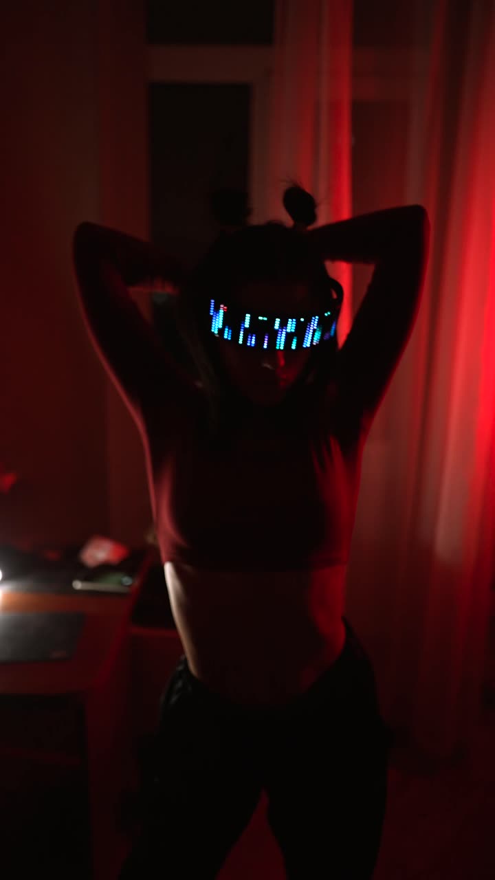 Donna con occhiali LED che balla in una stanza illuminata di rosso