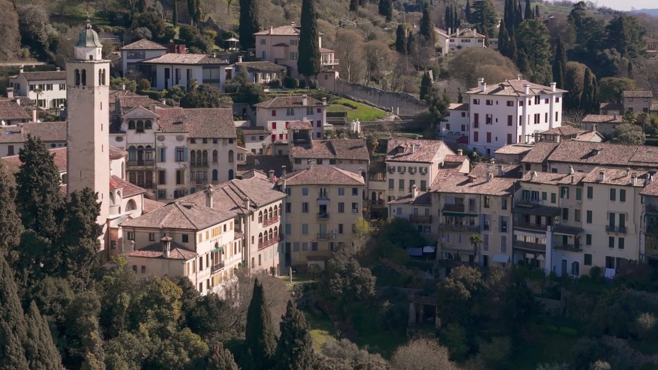 Edifici tradizionali di un borgo collinare italiano con campanile circondati dal verde.