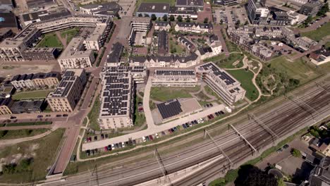 aerial showing dutch residential urban development and infrastructure of noorderhaven neighbourhood in zutphen, the netherlands, seen from above with rooftops full of solar panels along train tracks