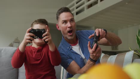 happy caucasian father with son sitting in living room and playing video games