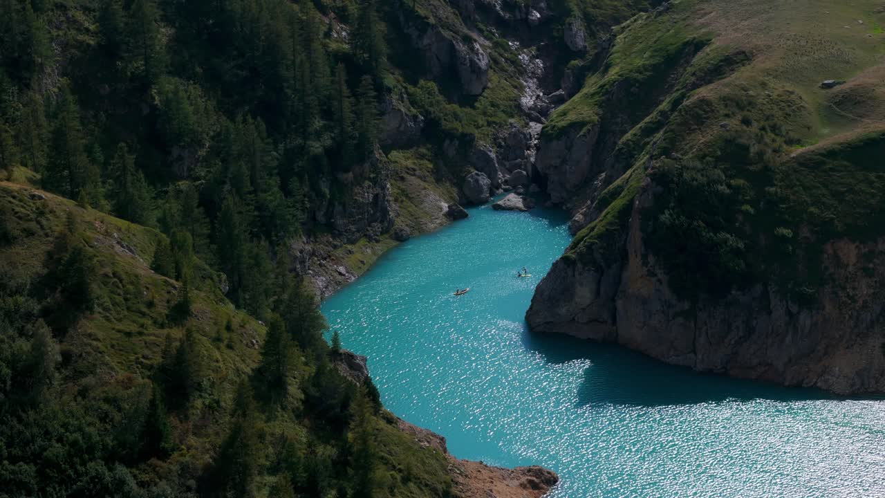 Veduta aerea di kayakisti che si godono le serene acque turchesi del Lago del Moncenisio, circondato da una vegetazione lussureggiante e scogliere rocciose