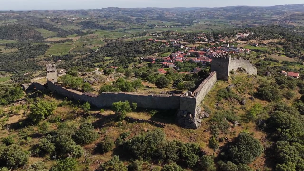 Ampie riprese aeree del Castello di Numão rivelano mura medievali, colline lussureggianti e un villaggio portoghese illuminato dal sole in un video cinematografico con drone.