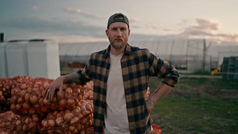 close-up portrait of a confident male farmer who is leaning on bags of onions that were collected during the harvest season from the farm