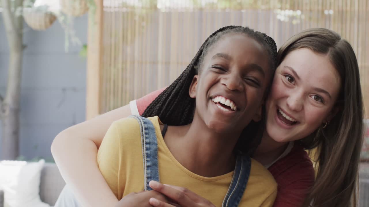 Portrait of happy diverse teenage female friends embracing and laughing at camera in slow motion