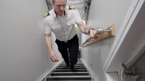 captain coming from ship engine room and walking up stairs towards camera