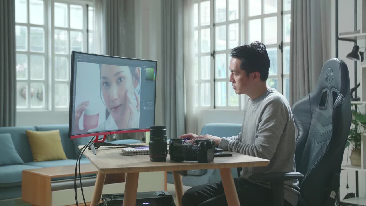 長袖のtシャツと黒いズボンを着たアジア人カメラマンが自宅で働いている間デスクトップコンピュータを使って写真を編集しています