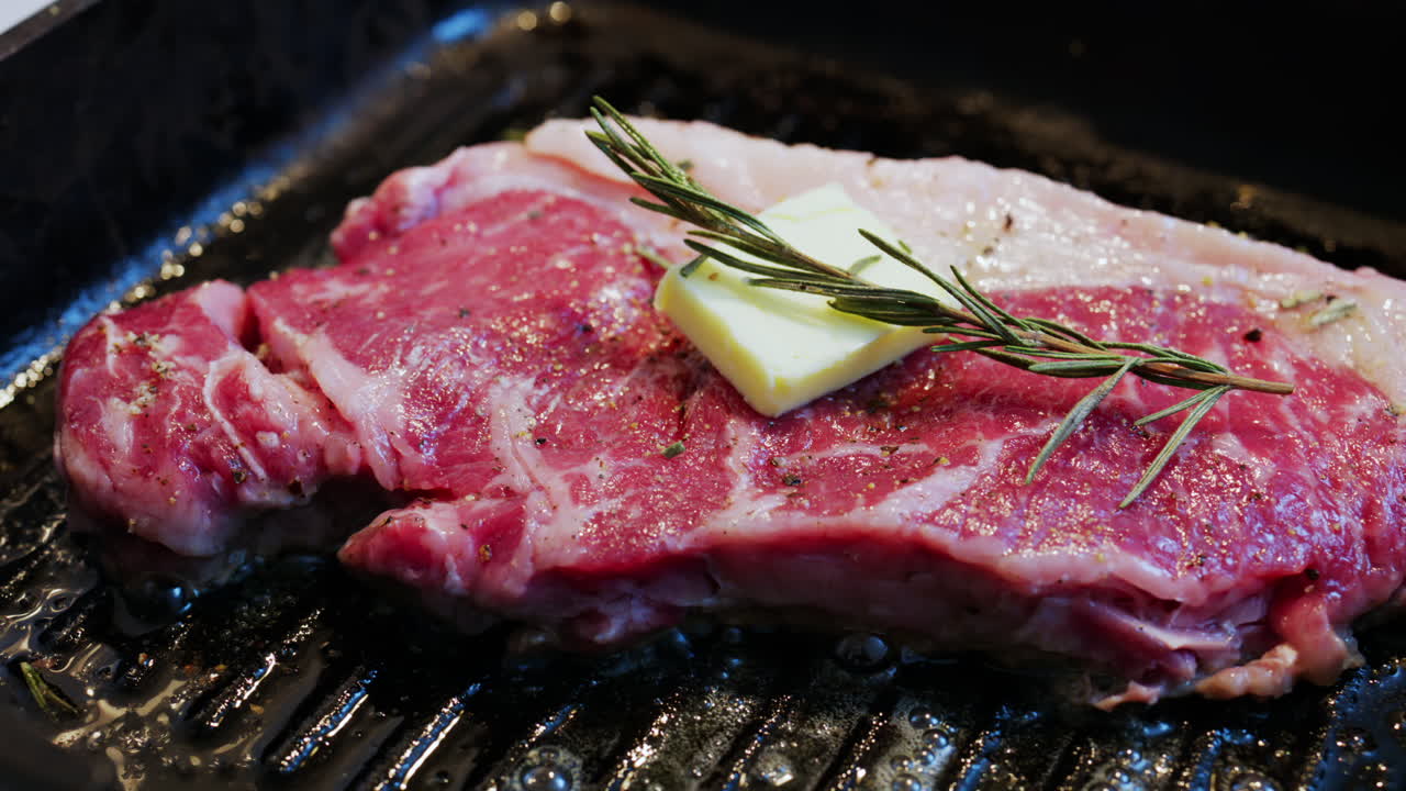 Burro che si scioglie su una bistecca condita che cuoce su una padella griglia calda con rosmarino