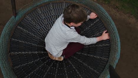 top down above young boy child sitting in round circular park swing