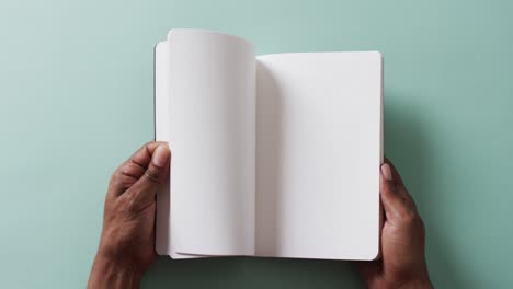 Close-up-of-hand-leafing-through-book-with-copy-space-on-green-background-in-slow-motion