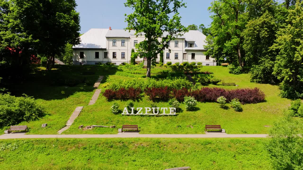 Historic Aizpute sign and local museum surrounded by summer greenery in Latvia