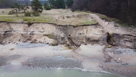 aerial view of baltic sea coast in overcast spring day, steep seashore dunes damaged by waves, coastal erosion, climate changes, revealing drone shot moving backwards