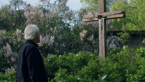 man contemplating at a wooden cross in a garden