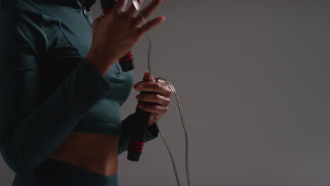 close up shot of female athlete wearing tracksuit training in gym fitness class with jump rope or skipping rope against plain background 1