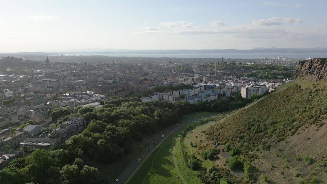 Aerial rise of Edinburgh city centre along the Holyrood Park edge of steep hill, Edinburgh, Scotland, UK