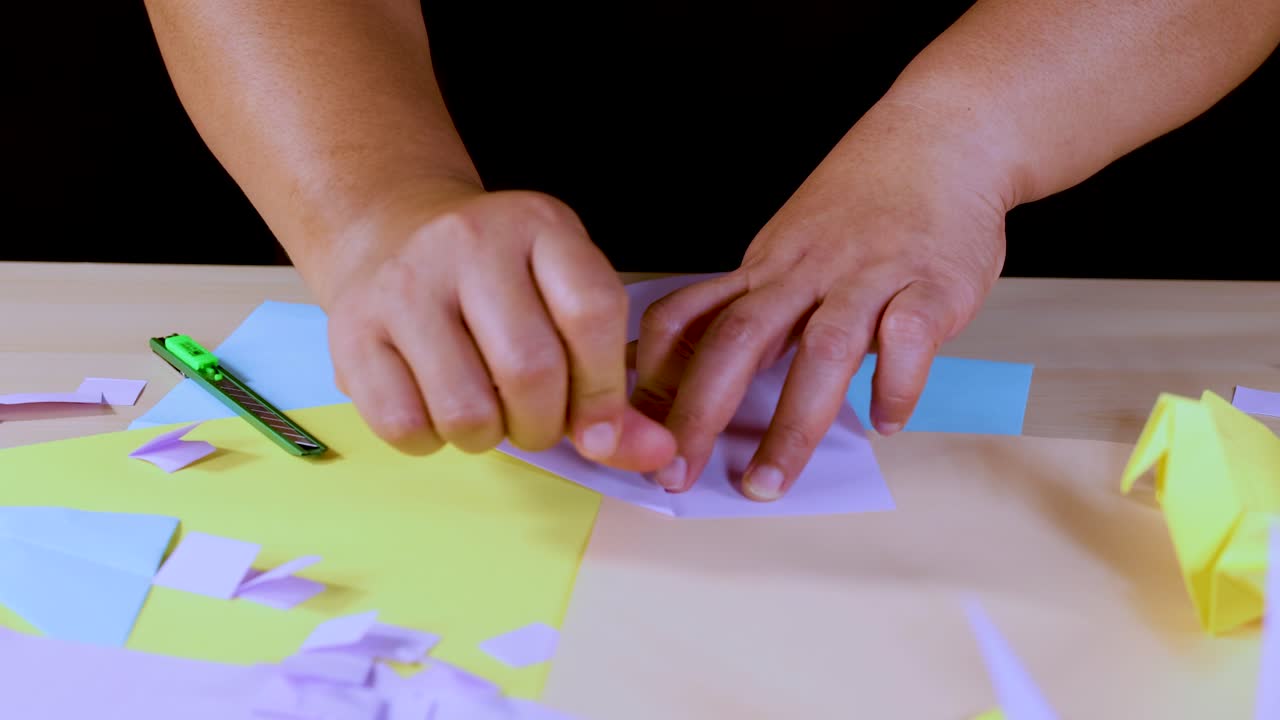 Person folds colored origami paper on table under bright lighting, close-up, steady overhead view