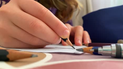 woman sits down at table carrying pencil and sketching in rough lines, coloring on paper, closeup on hands