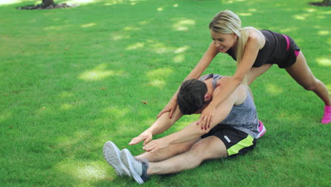 Woman-sport-trainer-help-fitness-man-stretching-legs-in-summer-park