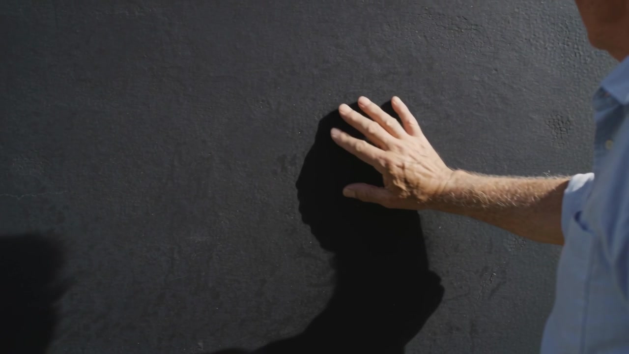 Entering right hand placing on matte black wall, adjusting shadow, light-blue shirt, copy space