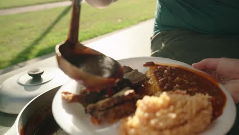 chef ladles bbq sauce over plate full of food on paper plate to patron at soup kitchen buffet