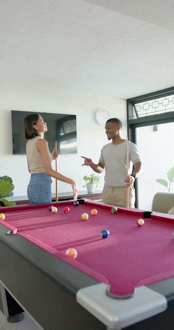 Vertical video: African American couple chatting at home, woman planning shot at red pool table
