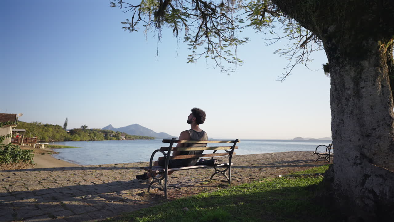 Lonely man sitting on waterfront relaxing and meditating at sunset