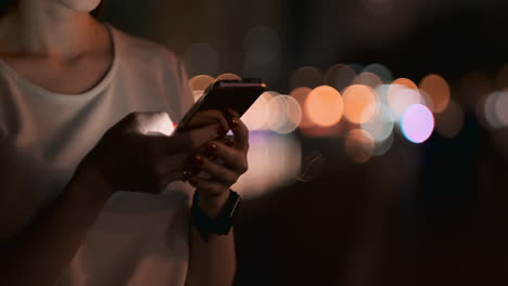 close-up of a mobile phone in the hands of a girl presses her fingers on the screen in the night city on the background of a beautiful bokeh. young businessman girl