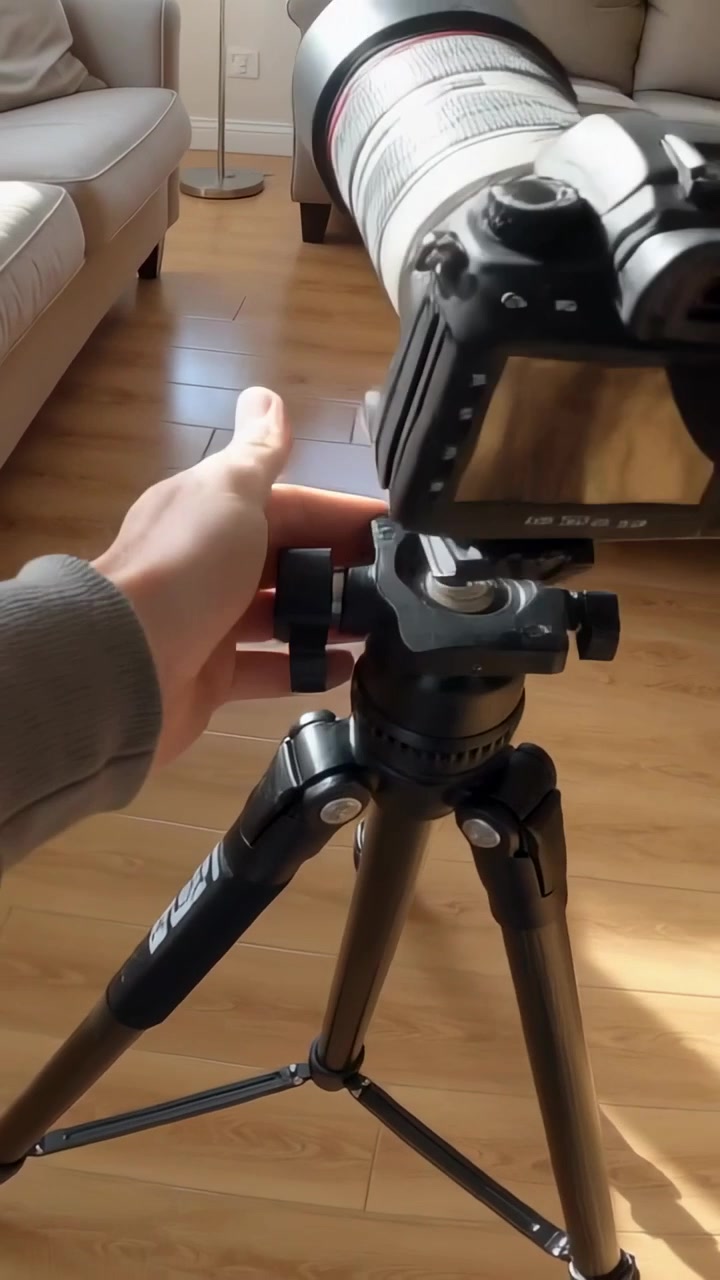 Vertikal video: Person i grå top nærmer sig stativ, monterer kamera med hvid linse derhjemme for at filme.