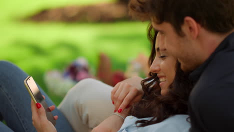 Smiling-girl-and-guy-lying-on-ground.-Cheerful-couple-using-phone-on-picnic