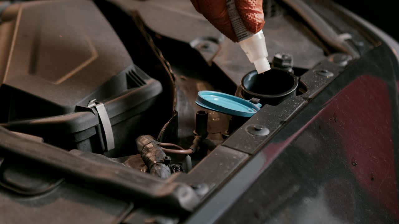 Hand pouring coolant liquid into car radiator reservoir inside engine bay