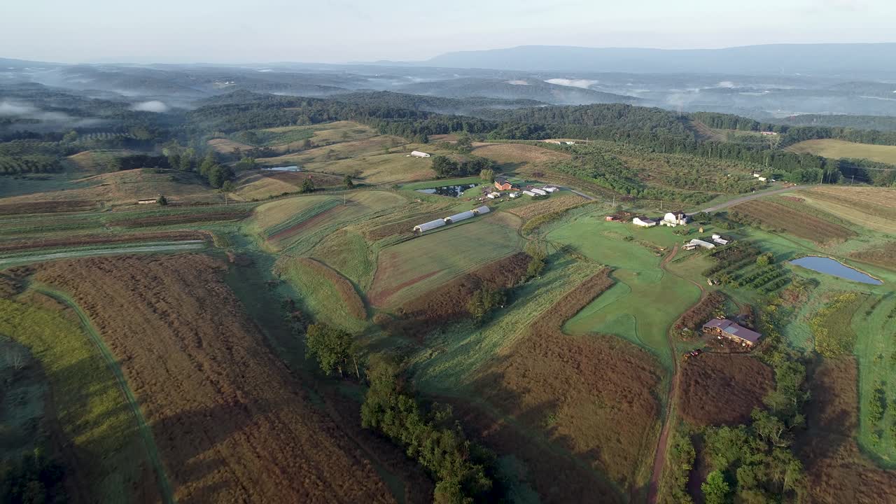 Aerial camera view of West Virginia countryside with farms, fields, mountains and fog settling in the valleys