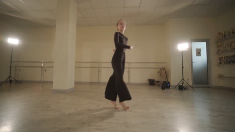 a group of young ballet students in black dancewear practicing positions in a spacious ballet studio with wooden flooring and wall-mounted barres. focused expressions and synchronized movements.