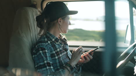 young woman sitting in van and using smartphone