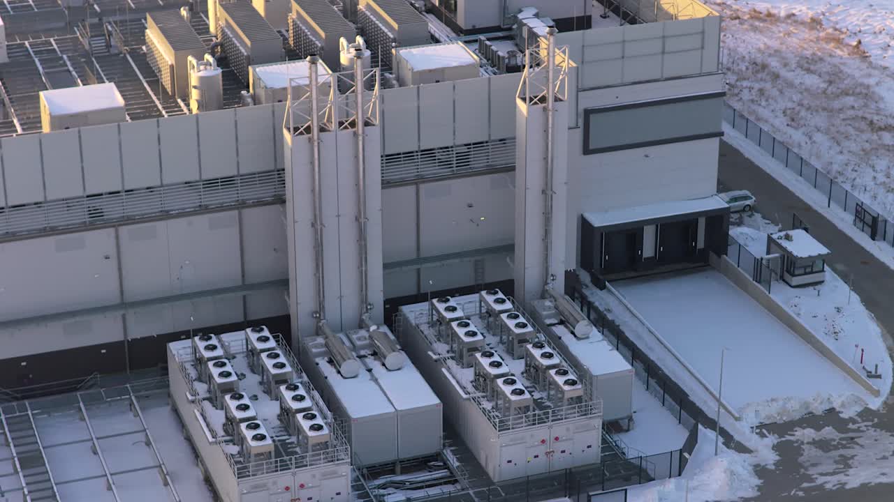 Industrial data center building with its cooling and ventilation systems covered in snow. An aerial orbit reveals the infrastructure