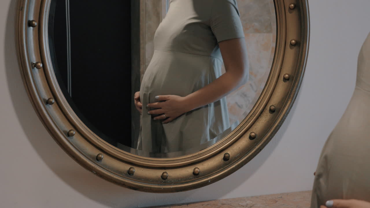 Una donna incinta che si guarda allo specchio e si accarezza la pancia