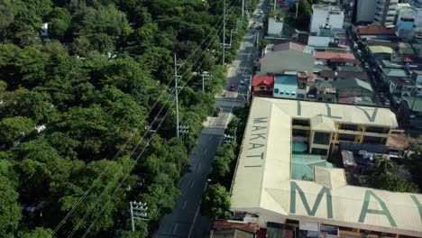 Drone-shot-of-Philippine-road-next-to-cemetery-full-of-trees-and-school-with-Makati-written-on-top