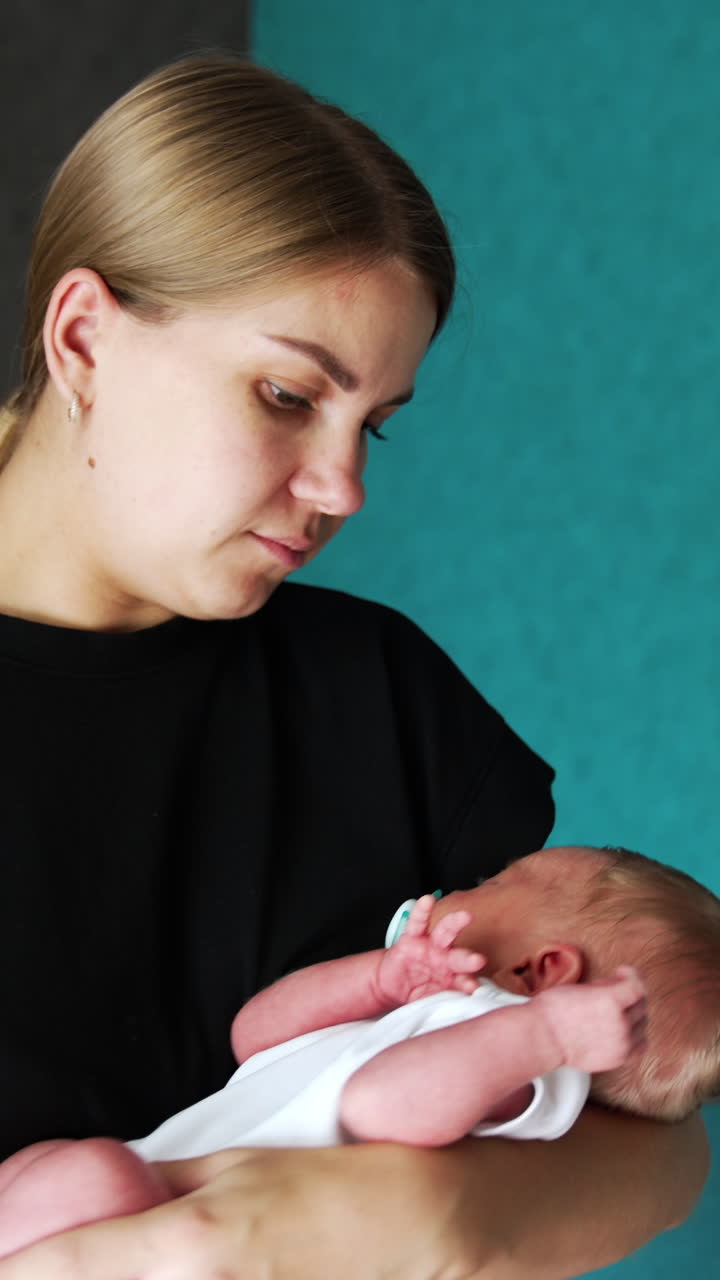 Caucasian woman wearing black t-shirt waving her baby. Loving mom looks at her newborn child with a smile. Vertical video