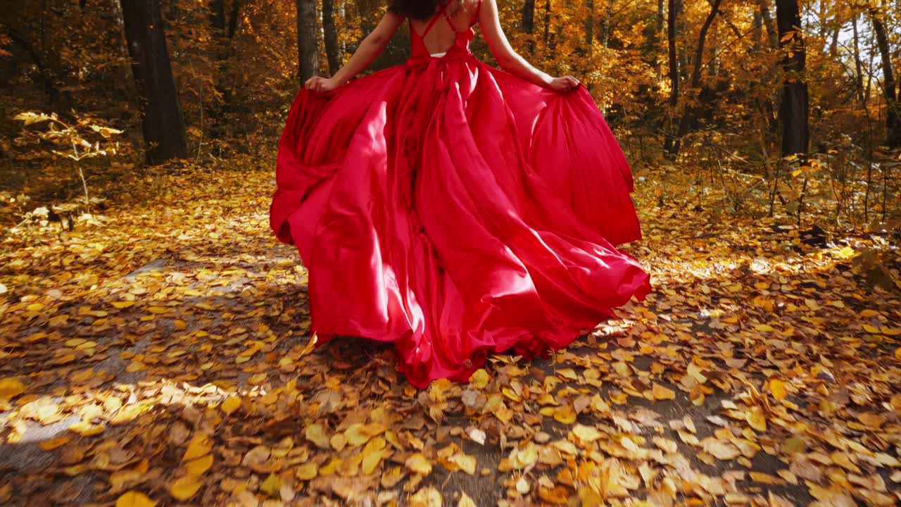A Woman in a Flowing Red Dress Walking Through a Vibrant Autumn Forest with Golden Leaves Carpeted on the Ground, Capturing Nature's Beauty in Every Step