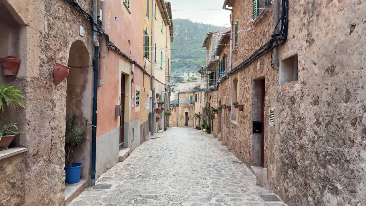 A narrow alleyway with a cobblestone street and a few potted plants in valldemossa majorca