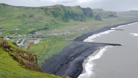 Statische-Landschaftsansicht-Der-Kleinen-Stadt-Vík-í-Mýrdal,-Island-An-Einem-Bewölkten-Tag,-Mit-Grasfeldern-Und-Schwarzem-Sandstrand