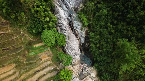 descending aerial shot of a people bathing in a lagoon at the bottom of a waterfall