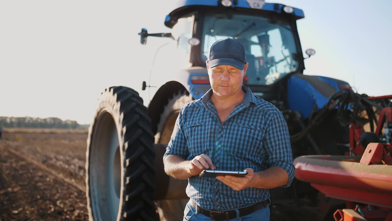 el agricultor está usando una tableta digital. en el campo de la granja, cerca del tractor, en el telón de fondo de la maquinaria agrícola. agricultura inteligente. tecnologías agrícolas