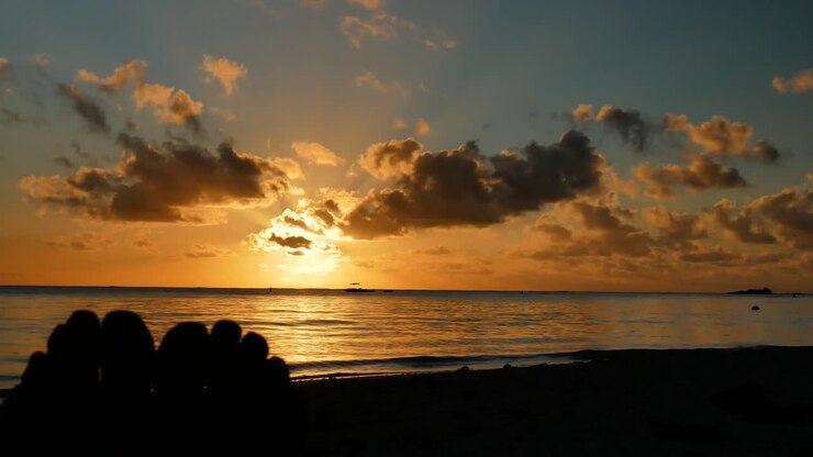 Una toma estática de un atardecer en una playa paradisíaca, con la silueta de un par de pies en primer plano a la izquierda.