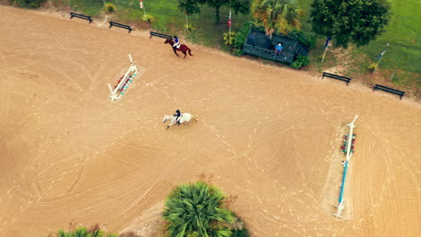 aerial view of professional equestrians horseback riding over hippodrome training field.