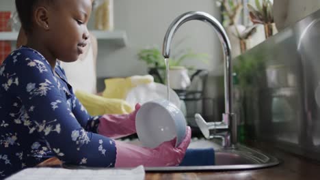 happy african american mother and daughter washing dishes in kitchen, slow motion