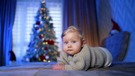 charming blond baby wearing grey sweater lies on the sofa. little child at home for christmas.