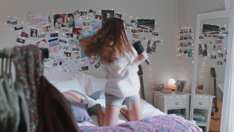 happy teenage girl dancing on bed at home to music enjoying celebrating weekend having fun singing wearing pajamas in bedroom