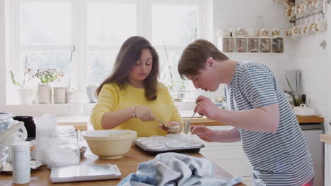 young downs syndrome couple putting mixture into paper cupcake cases in kitchen at home